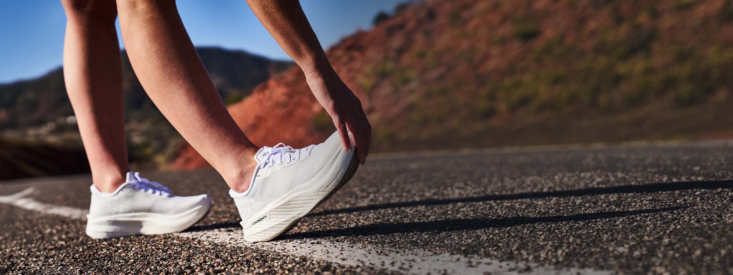 Person wearing white sneakers on a road with a blurred natural background