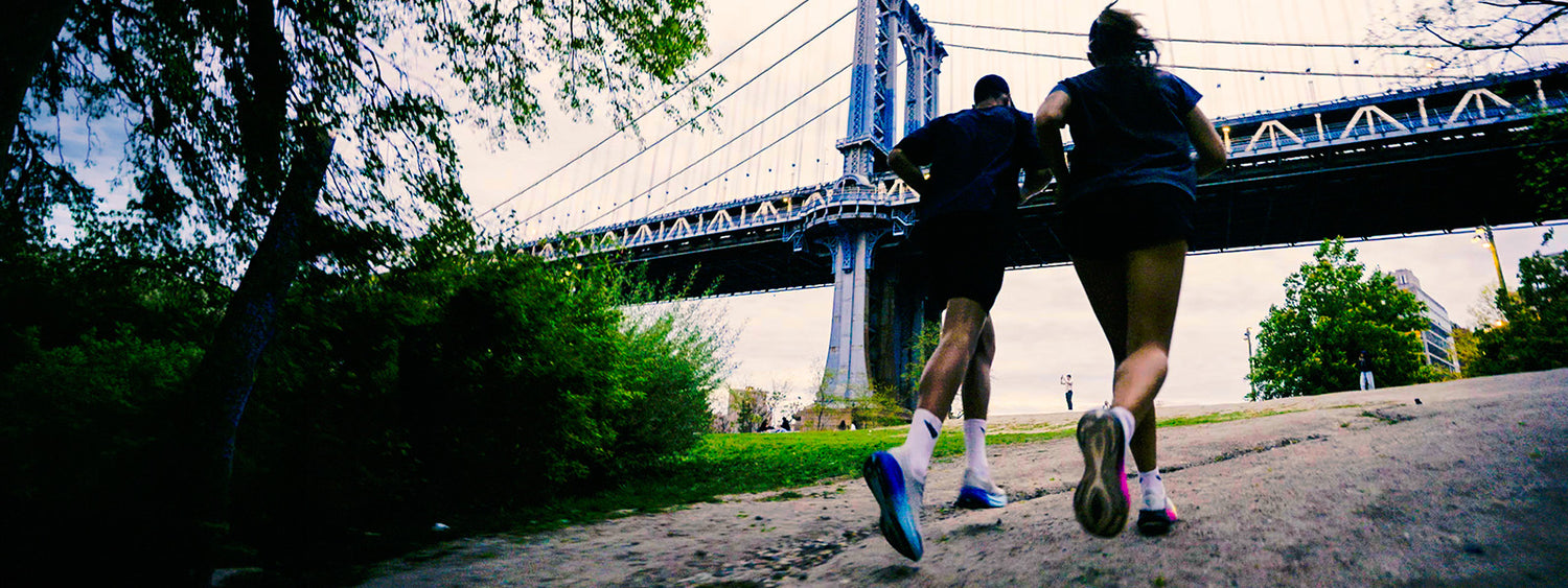 Two people running on a path with a bridge in the background