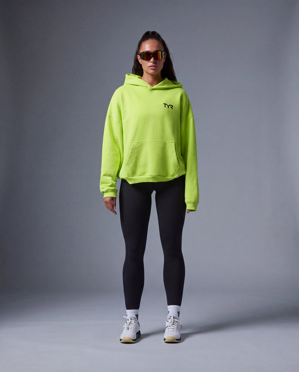 Model wearing oversized pullover hoodie, sunglasses, black joule elite leggings, and ambition cxt-3 trainers.
